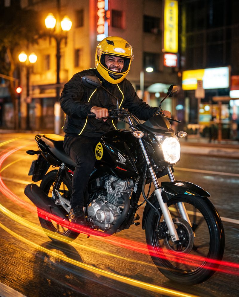 Piloto da iGO Motos sorrindo em uma moto adesivada com a marca iGO, à noite na cidade